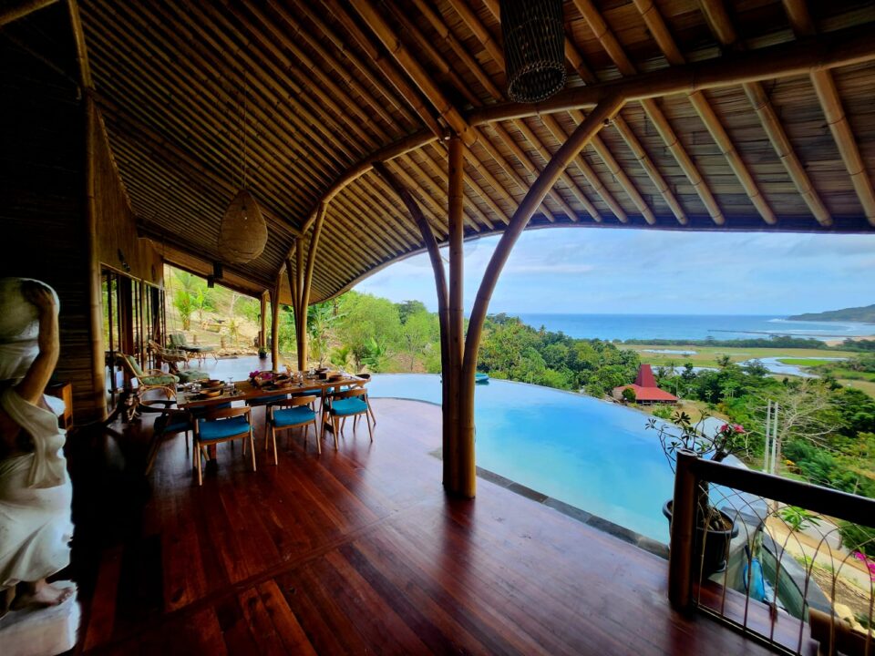 Salle à manger ouverte d'une villa en bambou avec piscine à débordement et vue panoramique sur la mer et les rizières de Sumba Indonésie, hébergement éco-luxe