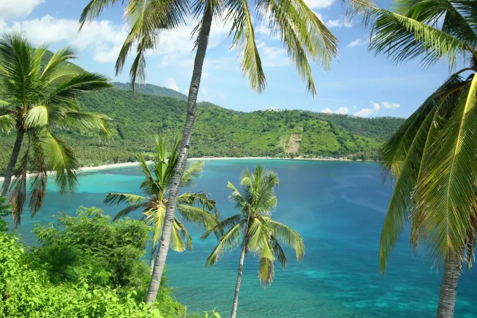 Baie aux eaux turquoise entourée de collines verdoyantes et de palmiers à Lombok – voyage sur mesure Lombok